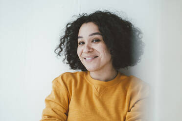 Smiling woman with curly hair in front of wall at home - JOSEF07851