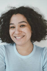 Happy beautiful woman with curly hair in front of wall - JOSEF07854