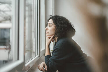 Thoughtful woman looking through window at home - JOSEF07866