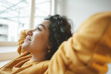 Thoughtful woman with hands behind head sitting at home - JOSEF07886