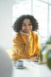 Happy woman with laptop sitting at table - JOSEF07899