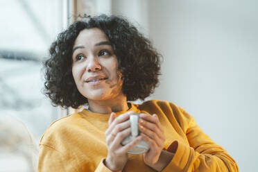 Thoughtful woman with curly hair holding coffee cup at home - JOSEF07903