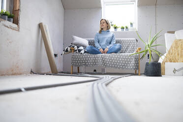 Nachdenkliche Frau sitzt auf dem Sofa im Dachgeschoss - HMEF01350