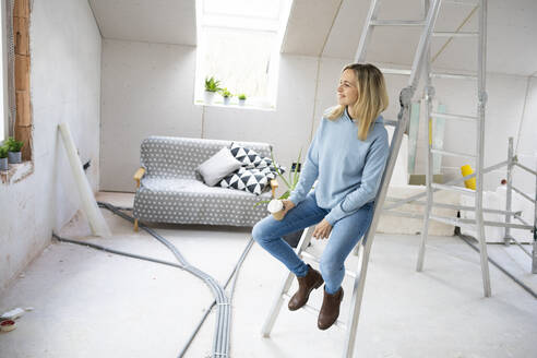 Nachdenkliche Frau mit Kaffeetasse auf einer Leiter im Dachgeschoss sitzend - HMEF01364