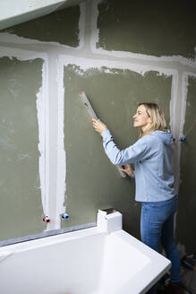 Blonde Frau misst Wand mit Wasserwaage in Loftwohnung - HMEF01368
