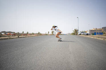 Frau mit Hut auf dem Skateboard an einem sonnigen Tag - FBAF01867