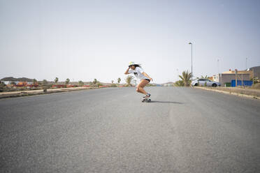 Woman with hat skateboarding on sunny day - FBAF01867