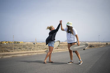 Friends with skateboard giving high-five to each other on sunny day - FBAF01869