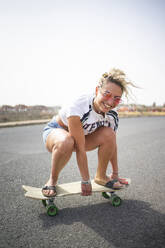 Glückliche junge Frau auf dem Skateboard an einem sonnigen Tag - FBAF01870