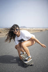 Frau mit zerzaustem Haar beim Skateboarden an einem sonnigen Tag - FBAF01871