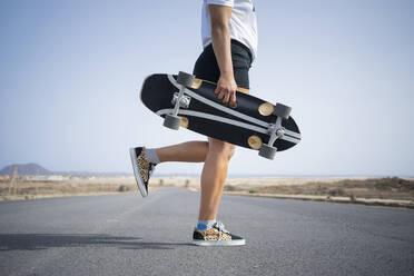 Frau mit Skateboard auf einem Bein stehend auf der Straße - FBAF01875