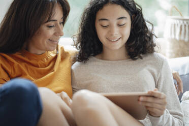 Smiling teenage girl using tablet PC by mother at home - JOSEF07906