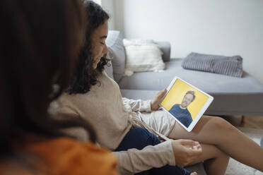 Happy teenage girl with mother having video call with father on tablet PC at home - JOSEF07911