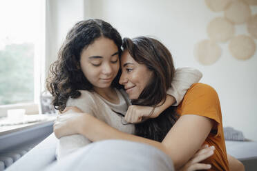 Teenage girl embracing mother sitting on sofa at home - JOSEF07915