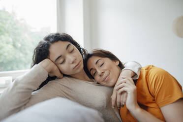 Teenage girl embracing mother and resting on sofa at home - JOSEF07920