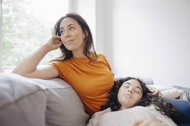 Thoughtful mother with daughter resting on lap at home - JOSEF07921