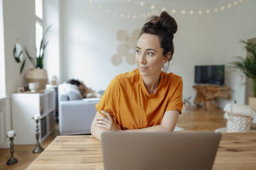 Thoughtful woman with laptop at dining table in living room - JOSEF07931