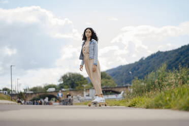 Teenage girl riding skateboard on street - JOSEF07933