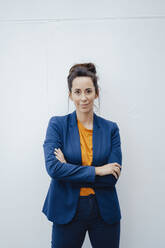 Confident businesswoman with arms crossed standing in front of white wall - JOSEF07941