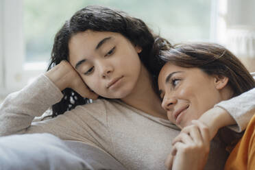 Teenager-Mädchen umarmt lächelnd Mutter sitzt auf Sofa zu Hause - JOSEF07954