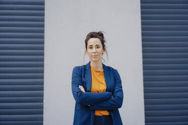 Businesswoman with arms crossed standing in front of gray wall - JOSEF07968