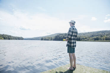 Man with fishing rod standing barefoot by riverbank on sunny day stock ...