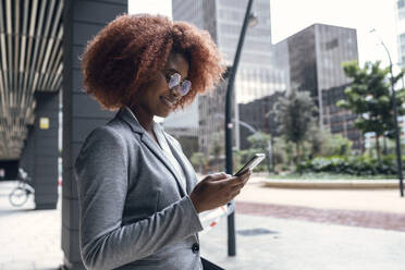 Junge Geschäftsfrau lächelt, während sie ihr Smartphone im Freien benutzt - JSRF01954
