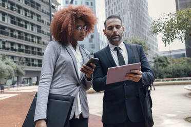 Businessman showing female colleague something on digital tablet - JSRF01958