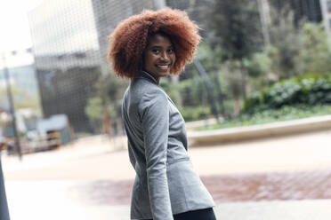 Portrait of young businesswoman looking over shoulder at camera with smile on face - JSRF01968