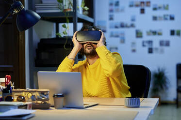 Businessman with laptop wearing virtual reality simulator in office - KIJF04405