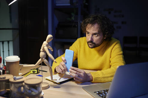 Geschäftsmann fotografiert die Figur eines Künstlers mit dem Handy im Büro - KIJF04417