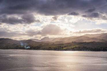 Landschaftlicher Blick auf das Meer mit Bergen im Hintergrund unter bewölktem Himmel bei Sonnenuntergang - SMAF02126