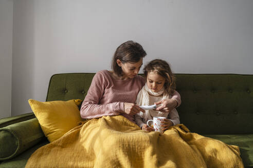 Mother checking temperature of sick daughter with thermometer at home - DIGF17728