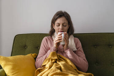 Sick woman with tea cup sitting on sofa at home - DIGF17730