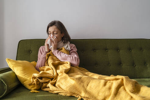Kranke Frau schnäuzt sich zu Hause die Nase mit einem Kosmetiktuch - DIGF17731