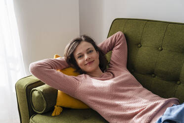 Lächelnde Frau auf dem Sofa liegend mit den Händen hinter dem Kopf zu Hause - DIGF17738