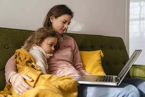 Mother with sick daughter consulting doctor online through laptop - DIGF17740