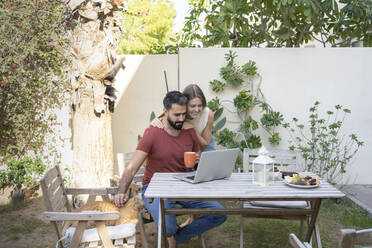 Mann benutzt Laptop mit Frau, die im Hinterhof steht - SVKF00010