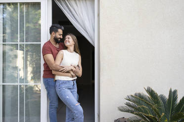 Happy couple looking at each other standing on doorway - SVKF00017