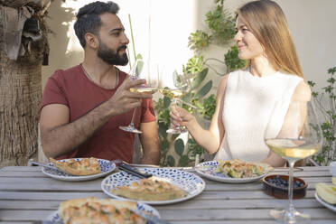 Couple toasting wineglasses sitting with savory pie in backyard - SVKF00020