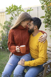 Frau mit Kaffeetasse auf dem Schoß eines Mannes im Garten sitzend - SVKF00025