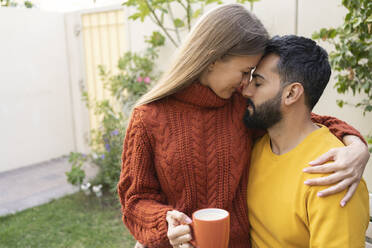 Frau mit Kaffeetasse sitzt mit Arm um Mann im Garten - SVKF00026