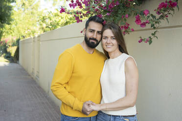 Smiling couple holding hands standing in front of wall - SVKF00027