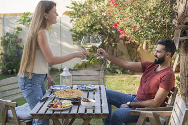 Couple toasting with wineglasses enjoying breakfast in garden - SVKF00038