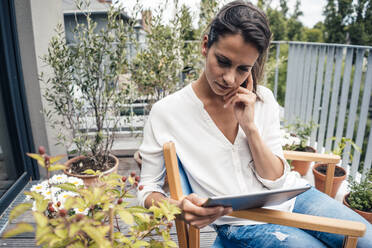 Frau schaut auf einen Tablet-PC auf einem Stuhl auf dem Balkon - JOSEF07995