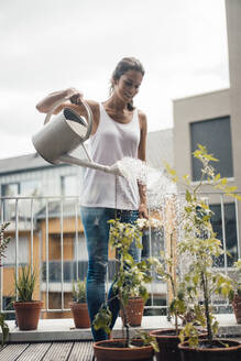 Smiling woman watering plants at balcony - JOSEF08011