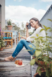 Smiling woman with eyes closed holding coffee cup sitting in balcony - JOSEF08012