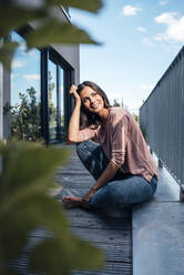 Happy beautiful woman sitting on balcony - JOSEF08029