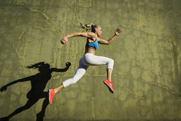 Young woman with fit body jumping and running against grey background.  Female model in sportswear exercising outdoors. stock photo