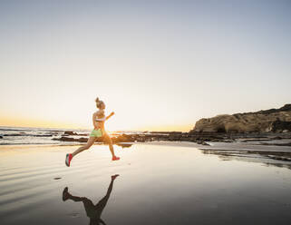 United States, California, Laguna Beach, Rear view of athlete woman running on beach at sunset - TETF01590